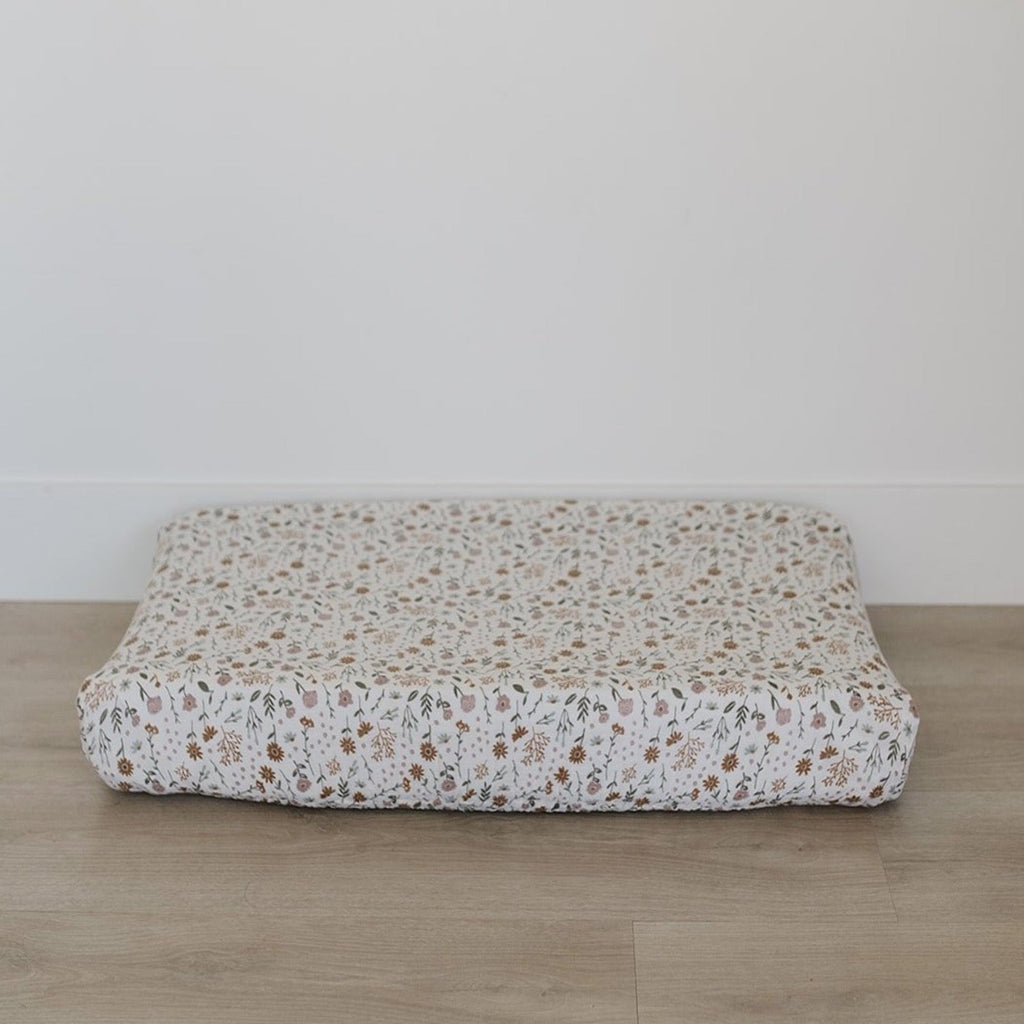 Meadow Floral Change Pad Cover by Mebie Baby on a change pad, in front of a white wall and on a wood floor. 