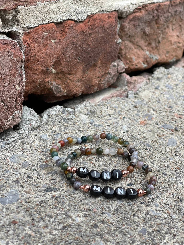 Mini Indian Agate Bracelets by Earth & Ether Co., laid on concrete in front of red brick wall. 
