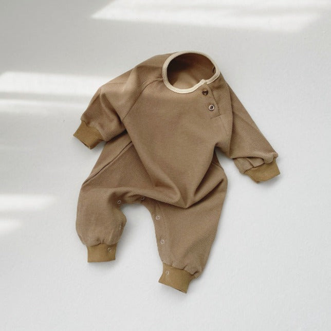 White background with the Mocha Romper by Mama Siesta, laying out. Romper is a mocha brown colour, with snap buttons at the left collar, and button closure in between the legs.