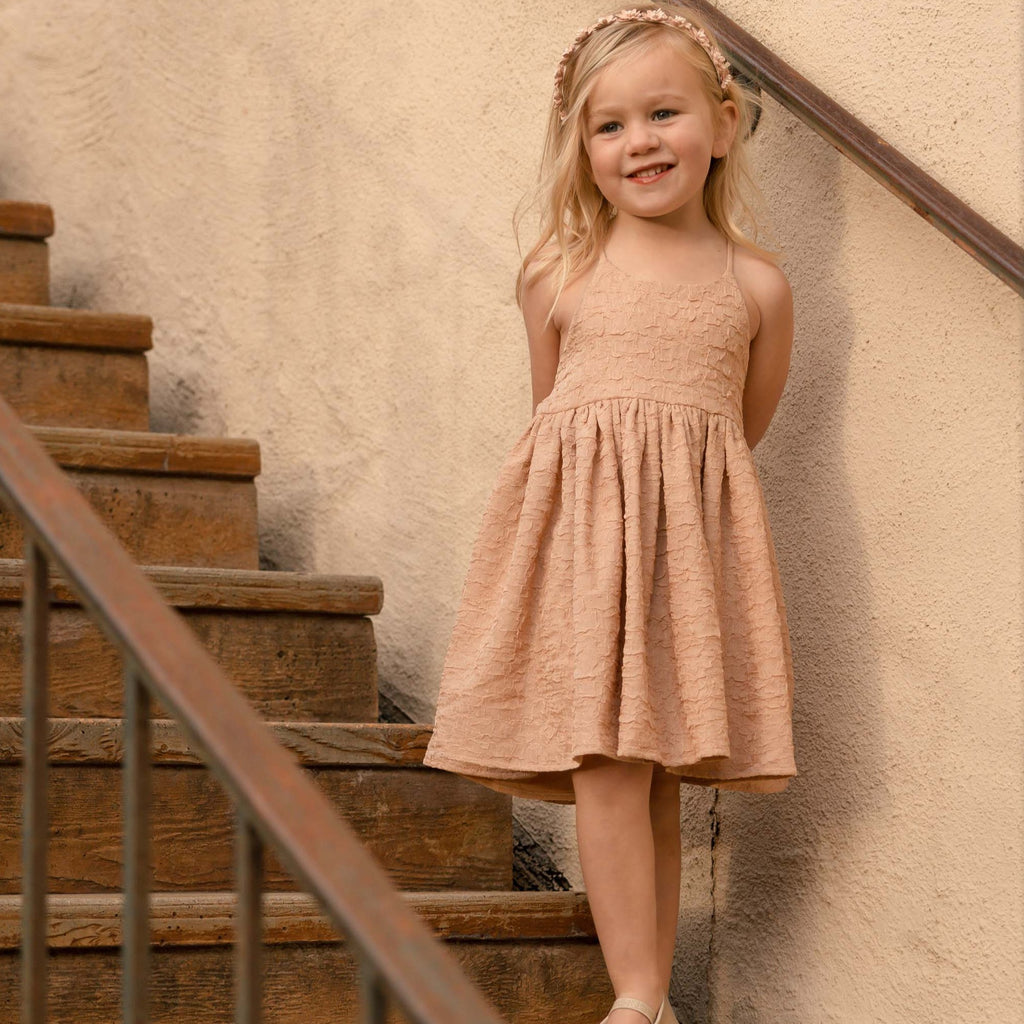 Model wearing Pippa Dress in Blush by Noralee, while standing on wooden stairs. 
