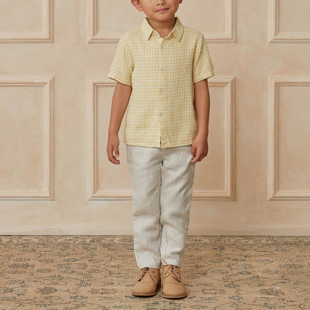 Beige wall with a little boy standing, wearing the Sebastian Pant by Noralee.