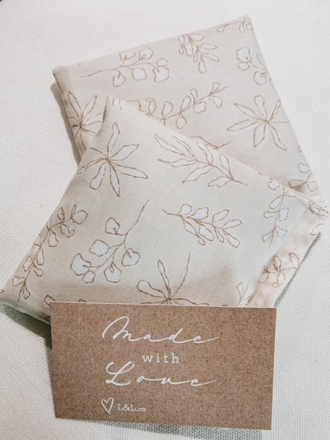 White background with 2 Boobie Bags in Natural Floral by L&L.co. Boobie Bag is a natural cream with white floral pattern, comes with 2 bags bundled together with twine.