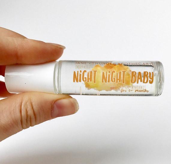 White background with hand holding a Night Night Baby - Baby Safe Essential Oil by Jane + Thunder. Text says "Night Night Baby" in orange.