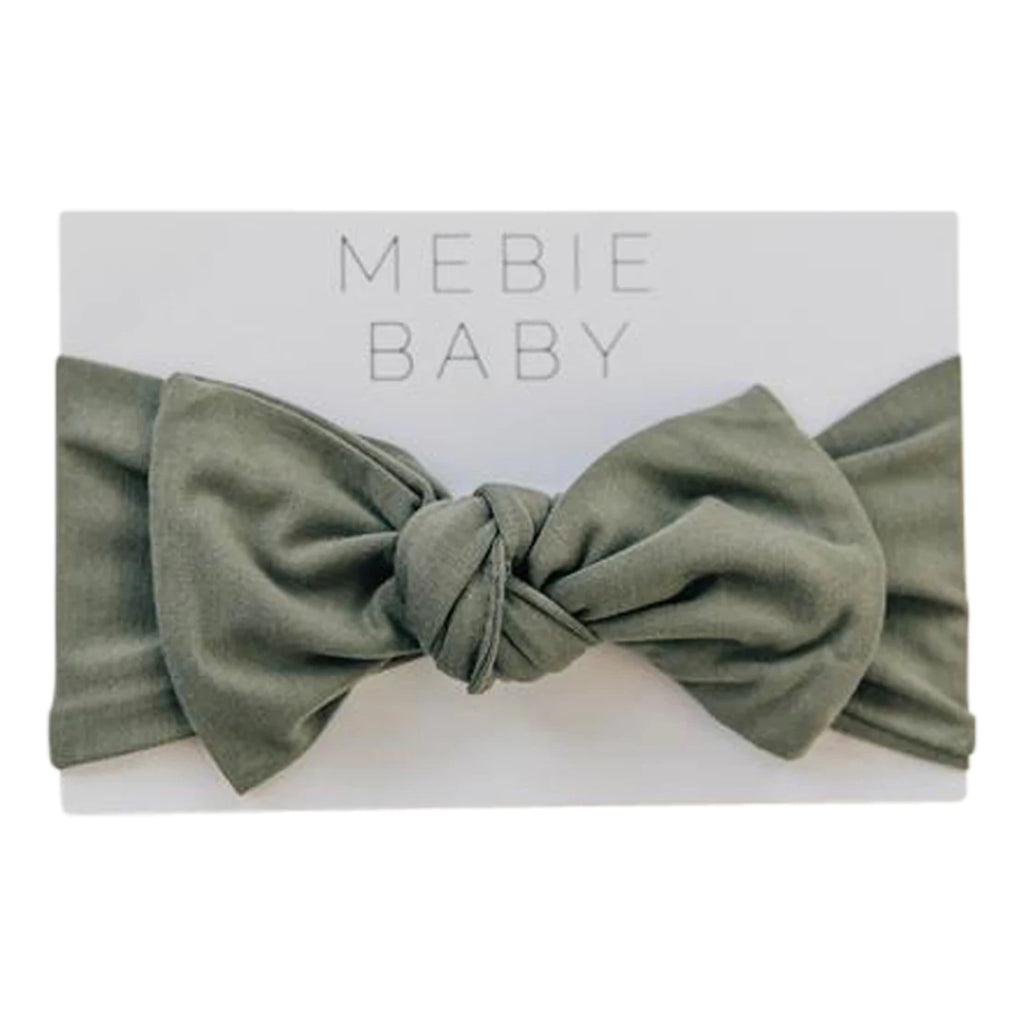 White background with the Olive Head Wrap by Mebie Baby in its packaging. Head wrap is olive with a tie in the front.