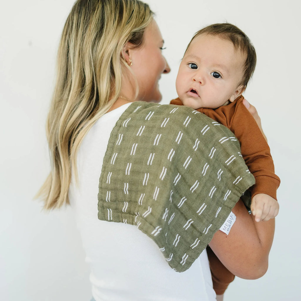 White background with mom facing wall, baby in her arms, and an Olive Strokes Burp Cloth by Mebie Baby over her shoulder.