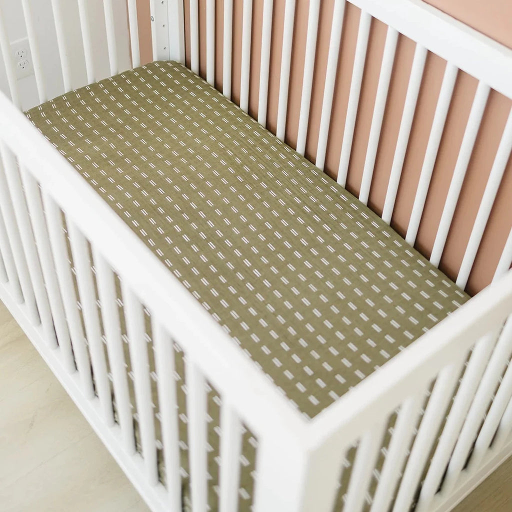 Overhead view from an angle of the Olive Strokes Crib Sheet by Mebie Baby on a mattress in a white crib.