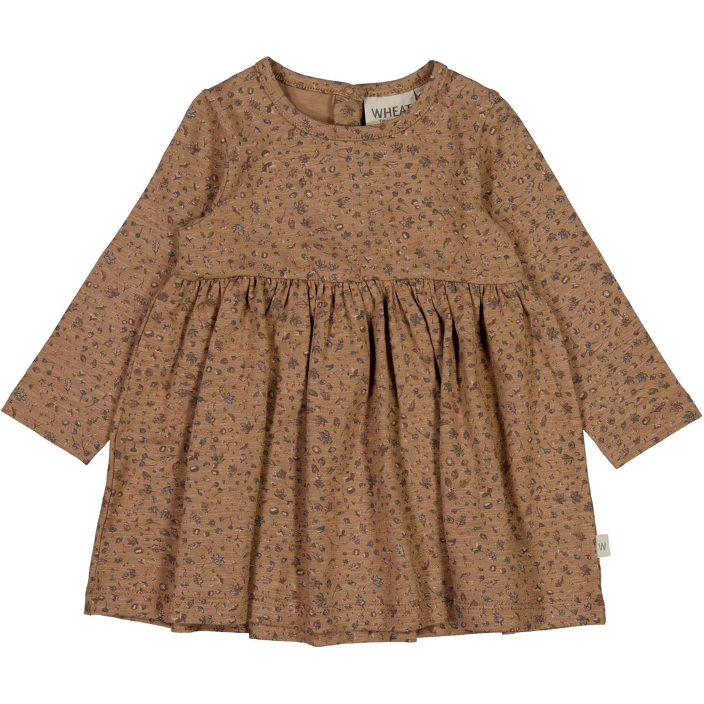 White background with Otilde Dress in Hazel Spruce & Cone by Wheat Kids Clothing. Dress is long sleeves with a cinched waist, that flows out, in a brown/hazel colour with spruce & cone print all over.