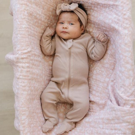 Overhead view of baby laying down down, wearing a Pale Pink Organic Cotton Footed Zipper One-Piece by Mebie Baby. One-Piece is a pale pink colour, with a zipper going down, and footies.