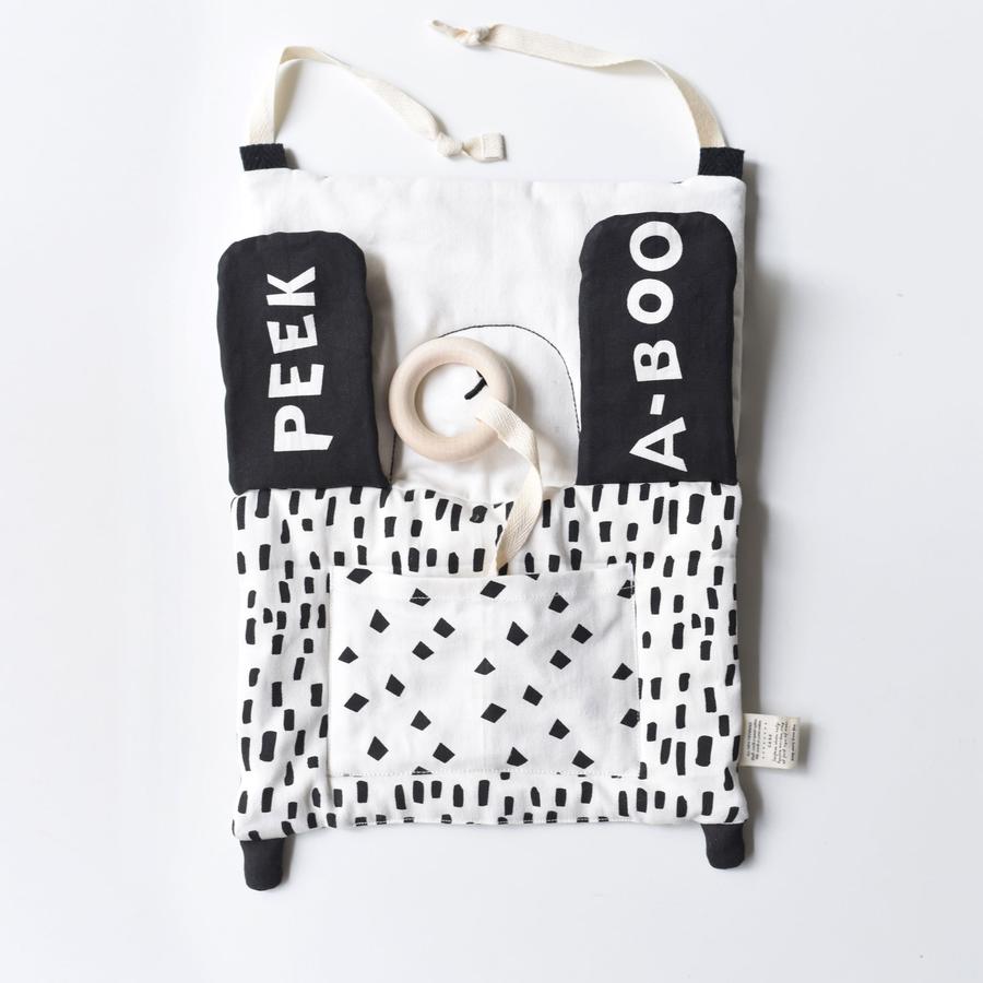 White background with the Peekaboo Panda Organic Activity Pad by Wee Gallery. Activity pad is black and white, and says Peek A Boo when the pandas arms are up, covering the eyes, and has a teething ring attached with canvas.