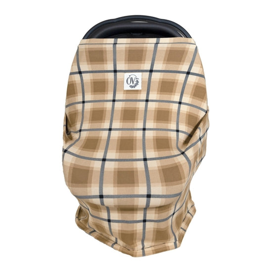 White background with a carseat and The Over Cover in Philip by The Over Company is on her car seat. This cover is a brown plaid pattern, with a white tag on the front with black font that says “OV” with greenery.