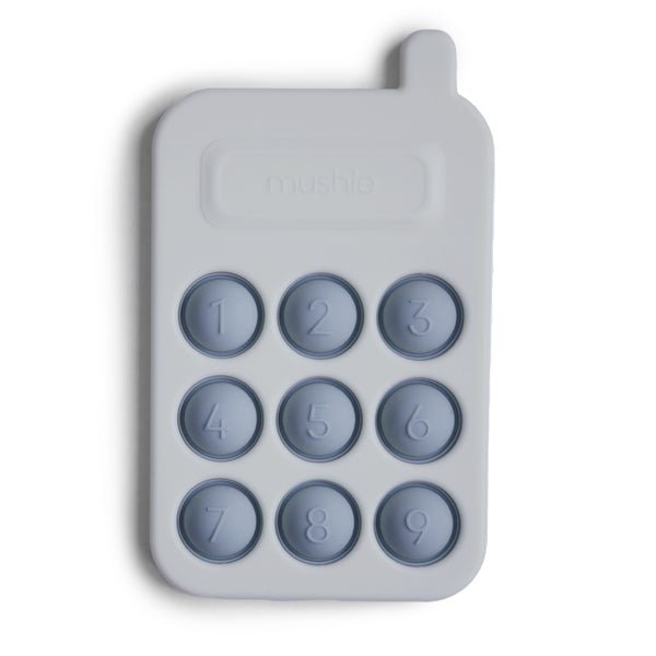 White background with Phone Press Toy in Tradewinds by Mushie. Toy is silicone and looks like a phone, it's grey blue with darker blue coloured number "pop its".