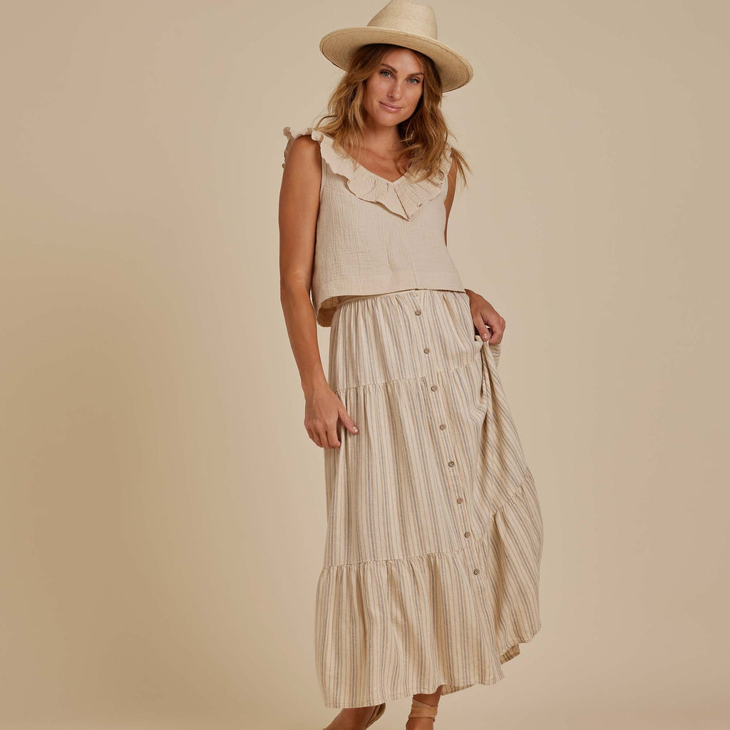 Model wearing the Joelle Skirt by Rylee and Cru in Rustic Stripe, with a Natural coloured crop top by Rylee and Cru with a straw hat. Model standing in front of beige wall. 