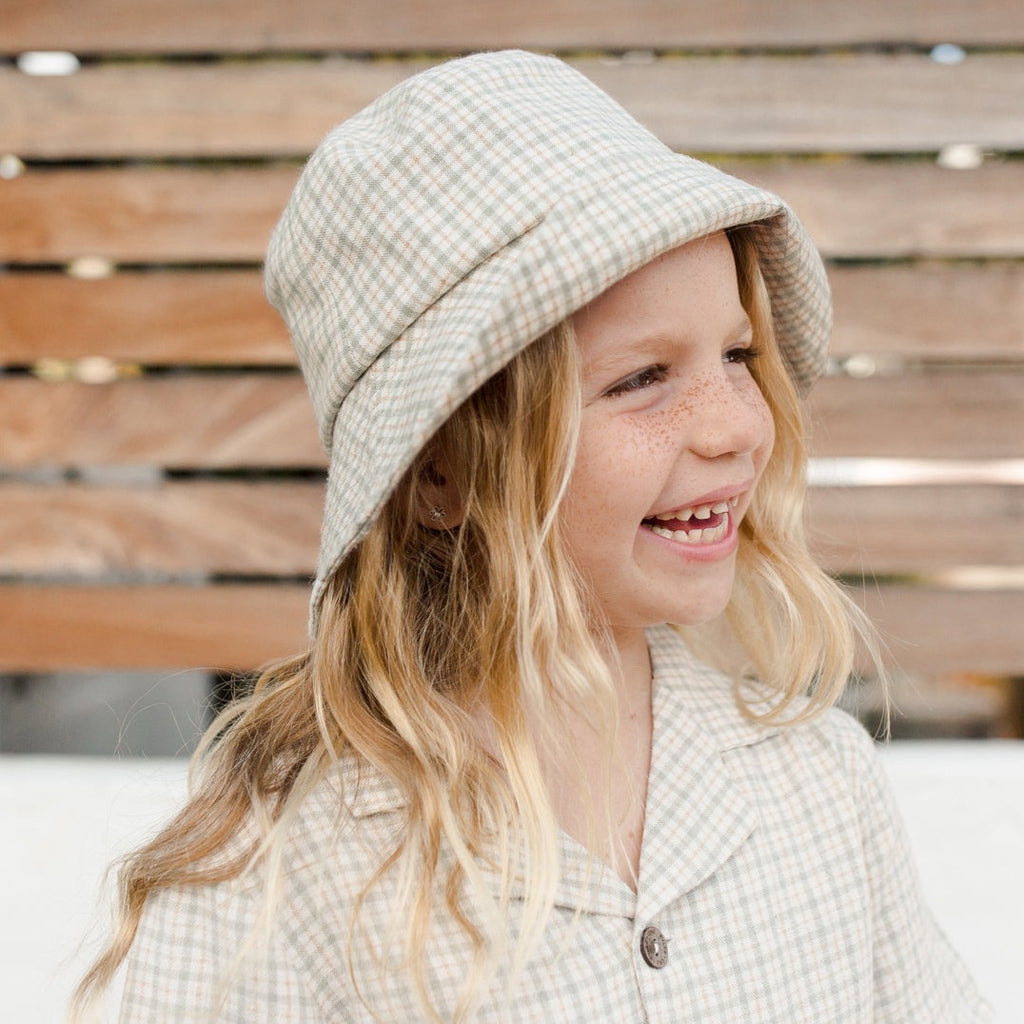 Model wearing Beach Bucket Hat in Green Laurel Plaid by Rylee and Cru, with a matching top in front of a wood fence. 