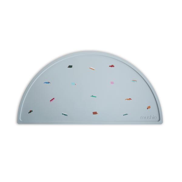White background with Silicone Place Mat in Retro Cars by Mushie. Placemat is a sky blue with colourful retro cars, made of silicone, and in a semicircle.