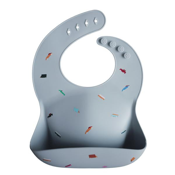 White background with a Silicone Bib in Retro Cars by Mushie. Bib is a sky blue colour with colourful retro cars, with a deep pocket on the front, and a rounded neck fastener at the back.