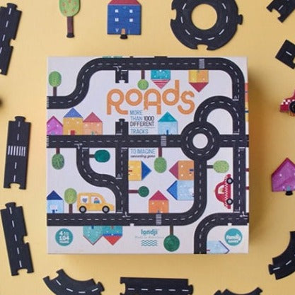 Yellow background with Roads Game by Londji. Shows the box it comes in, and the road maps laid out around it.