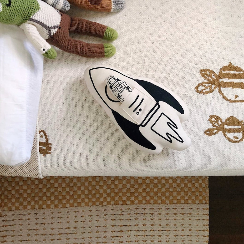 Overhead shot of a bed with Rocket + Astronaut Pillow by Imani Collective. Natural canvas with black accents in the shape of a rocket, with a mini astronaut as well.