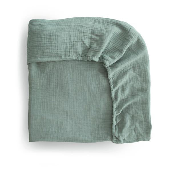 White background with a folded Extra Soft Muslin Crib Sheet in Roman Green by Mushie on it. Roman Green is a eucalyptus green.
