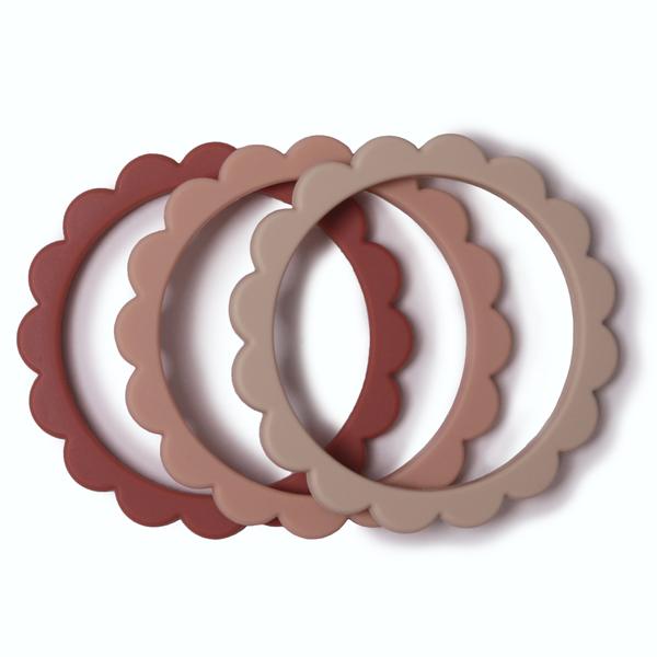 White background with Flower Teething Bracelet 3-Pack in Rose/Blush/Shifting Sand by Mushie. These are round bracelets, that look like flower petals - comes with a rose, blush, and beige colour bracelet.
