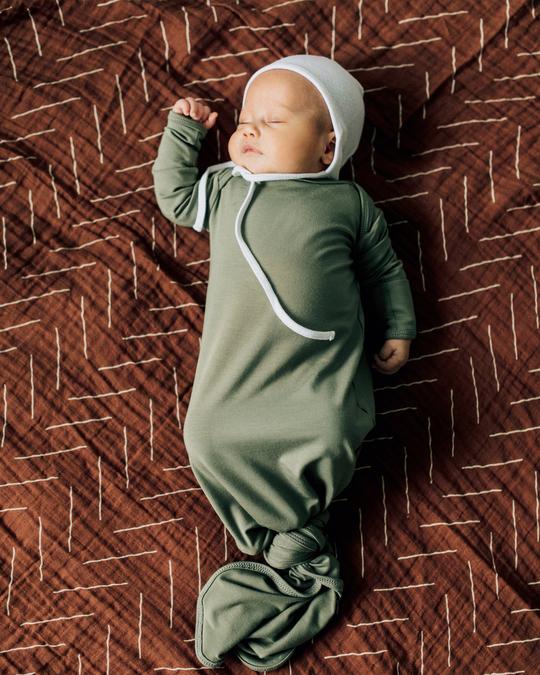 Overhead view of baby laying down and sleeping on a Rust Mudcloth Muslin Swaddle by Mebie Baby.