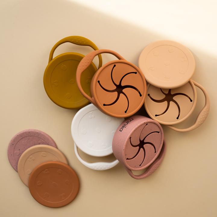 Beige background with an overhead view of a pile of Silicone Snack Cups with Lids by Minika.
