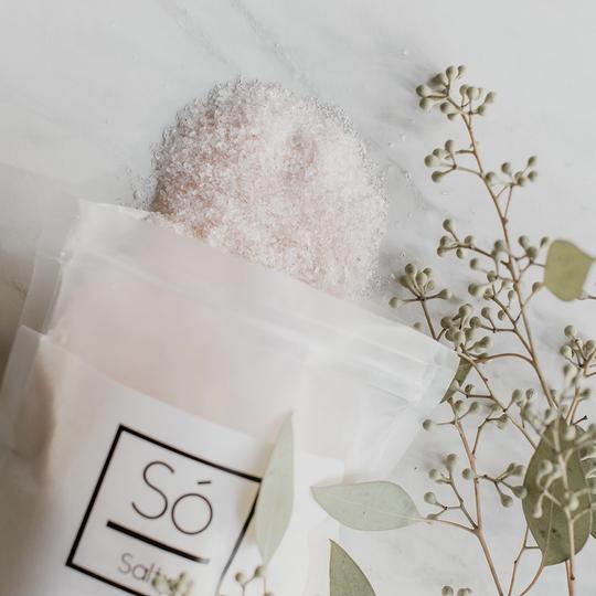 White marbled table with eucalyptus laid out, and the Salty in Eucalyptus Rose by So Luxury Bath and Body Inc. open, and coming out of the package.