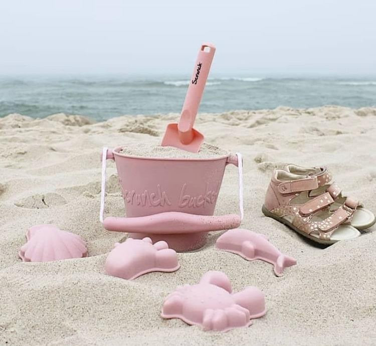 The Scrunch Bucket & Spade in Blush by Scrunch Kids in the sand, with the water behind.