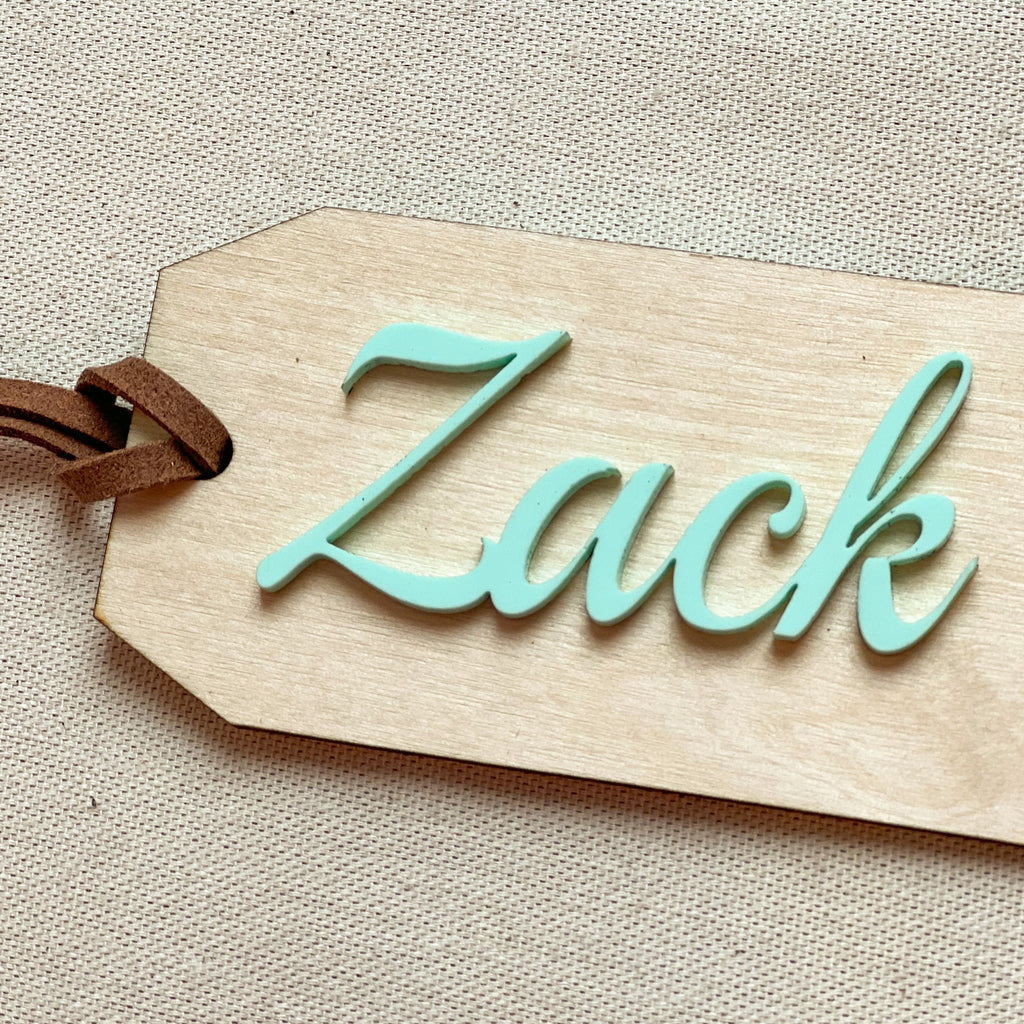 Customized name tag in Seafoam with the name Zack on a beige surface. 