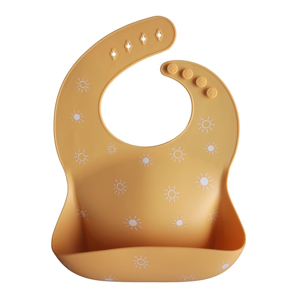 White background with a Silicone Bib in Sun Orange by Mushie. Bib is an orangey yellow with white suns all over, with a deep pocket on the front, and a rounded neck fastener at the back.