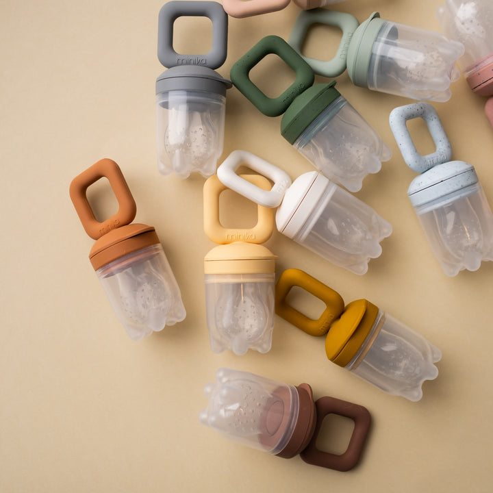 Beige background with overhead view of a pile of Silicone Feeder Teethers by Minika.