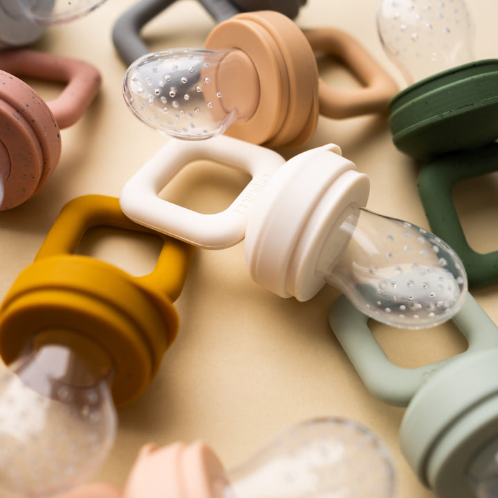 Beige background with overhead view of a pile of Silicone Feeder Teethers by Minika.