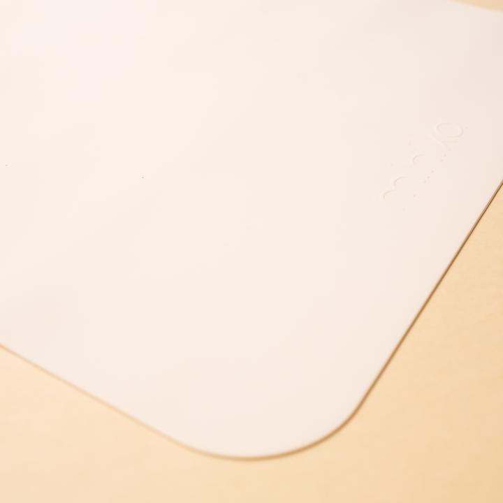Beige background with a Silicone Placemat in Shell by Minika. Placemat is square silicone, in a white colour.