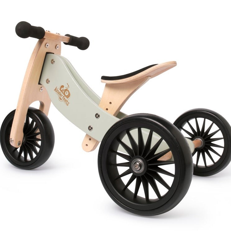 White background with side view of Tiny Tot Balance Bike in Silver Sage by Kinderfeets. Bike is a natural wood, with Silver Sage details, black wheels, black handles, and a black seat.