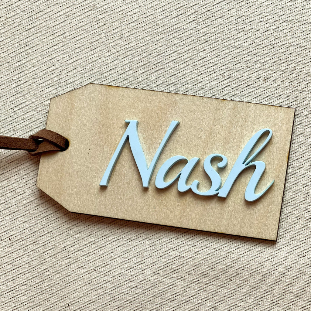 Customized name tag in Sky with the name Nash on a beige surface. 