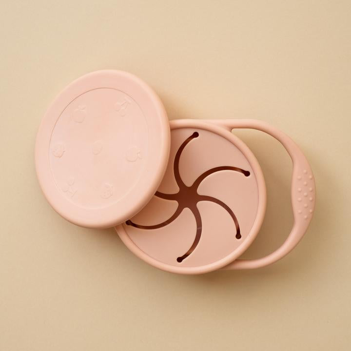 Beige background with a Silicone Snack Cup in Blush by Minika. Snack cup has a small handle to carry, and a lid as well, all in the colour blush.