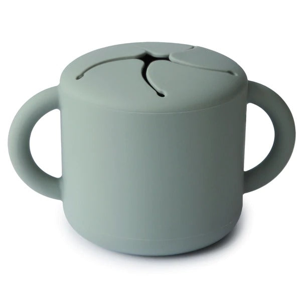 White background with Silicone Snack Cup in Cambridge Blue by Mushie. Snack cup has 2 handles, and a spill proof top, in a light blue/green colour.