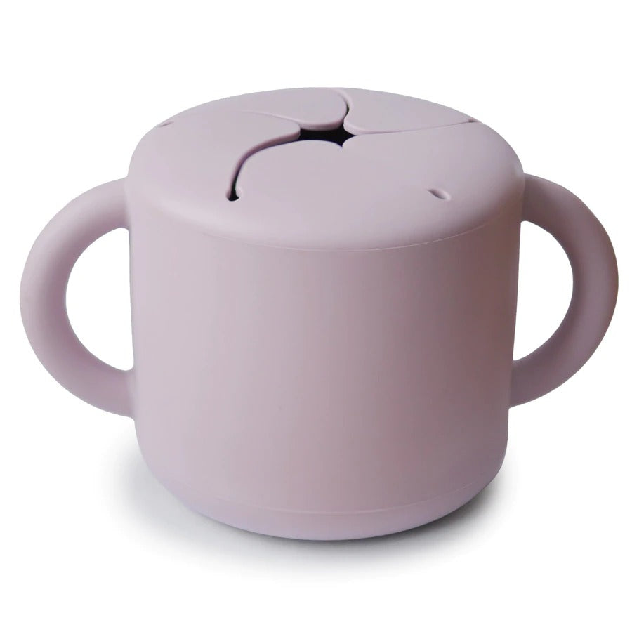 White background with Silicone Snack Cup in Soft Lilac by Mushie. Snack cup has 2 handles, and a spill proof top, in a light purple colour.