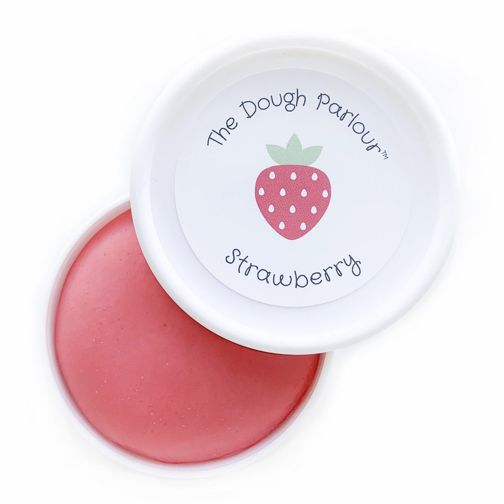 White background with Strawberry Play Dough by Dough Parlour, open slightly to show colour. Play dough comes in a white container, is red, and has a sticker on the top that says "Strawberry".