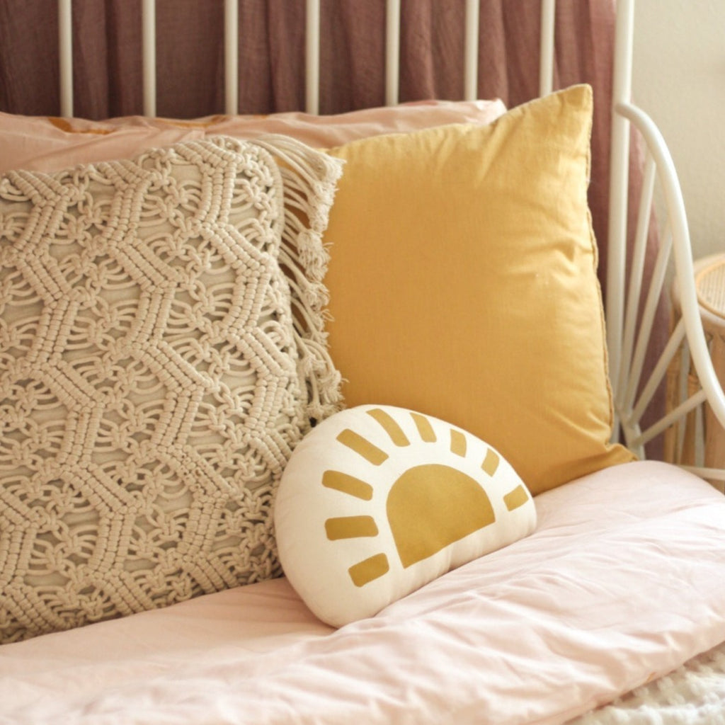 White wrought iron bed with pillows on it, and Sunshine Pillow by Imani Collective. Semi Circle pillow thats white canvas with mustard sun.