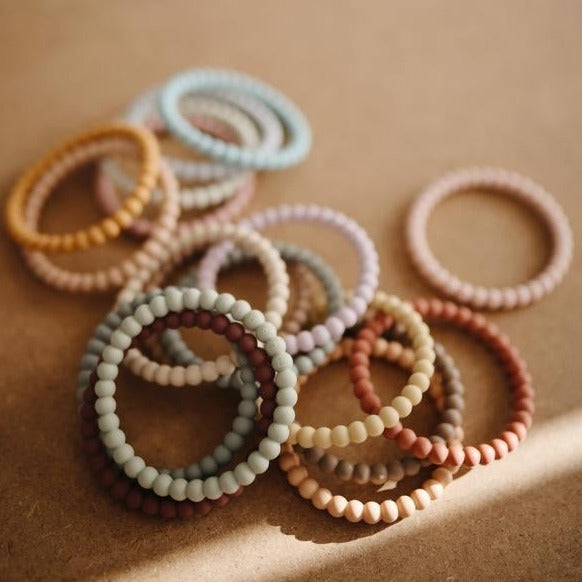 Brown background with a pile of the Pearl Teething Bracelets by Mushie.