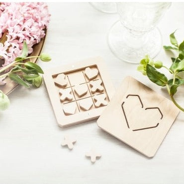 Flat lay with open box of heart tic tac toe game with flowers, and greenery.