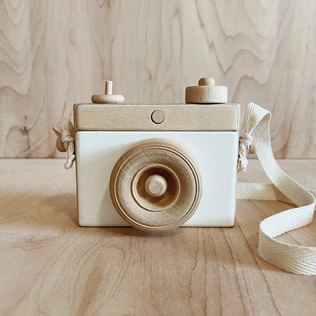 Wood background with Wooden Camera in White by Little Rose & Co. Camera is wood with white accents, and a canvas strap.
