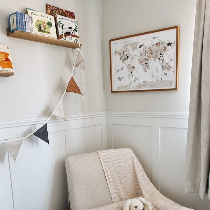 Corner of a nursery with a chair, and a World Map Fine Art Print by Little Roglets on the wall.