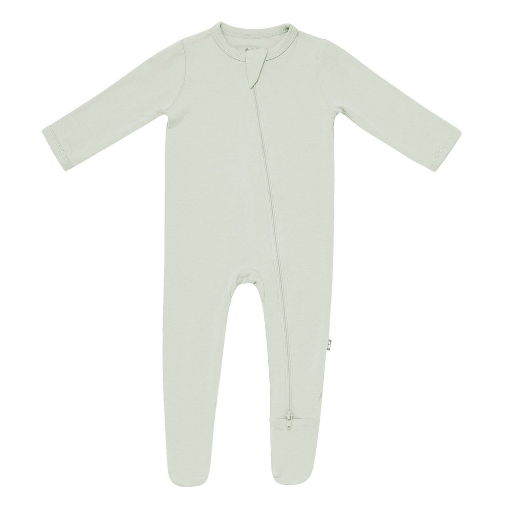 White background with Zippered Footie in Aloe by Kyte Baby. Zipper footie is a pale green, almost neutral, with a zipper that runs all the way along the front.