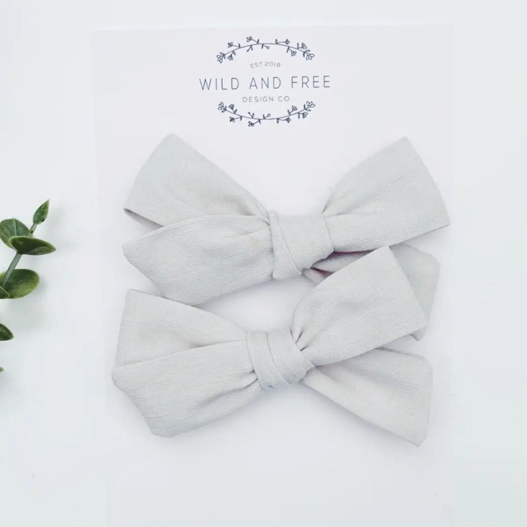 White background with the Sand School Girl Pigtail Bow Set by Wild and Free Design Co. in its packaging. Bows are thin, in an oatmeal colour.