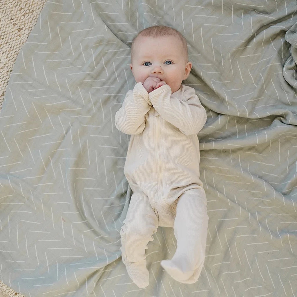 Overhead view of baby laying on a Desert Sage Muslin Quilt by Mebie Baby. Quilt is pale sage with white lines all over.