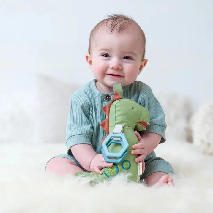 Model holding Bitzy Bespoke Link & Love™ Activity Plush with Teether in Dino Toy by Itzy Ritzy, white background. 
