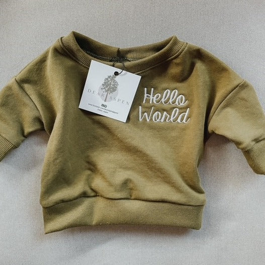 Grey background with Hello World Crewneck in Meadow by Dear Aspen. Crewneck is an olive green colour with "Hello World" embroidered in white on the left chest.