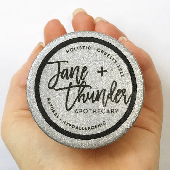 White background with hand holding a Whipped Body Butter by Jane + Thunder.