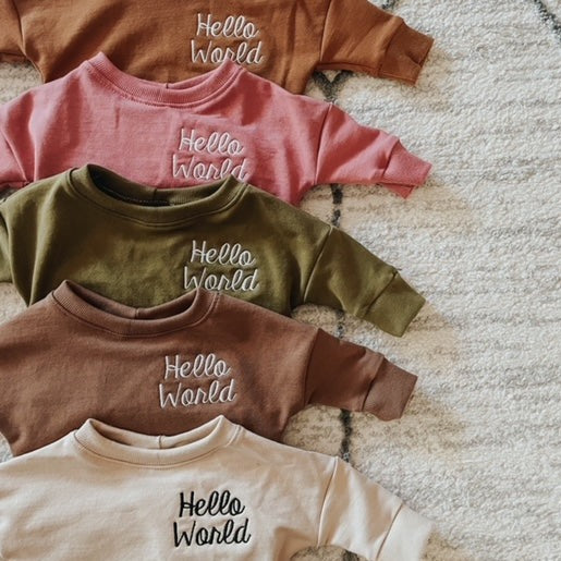 Overhead view of Hello World Crewnecks by Dear Aspen, stacked in a row.